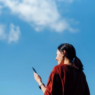 Jeune femme consultant son smartphone devant un ciel bleu.  