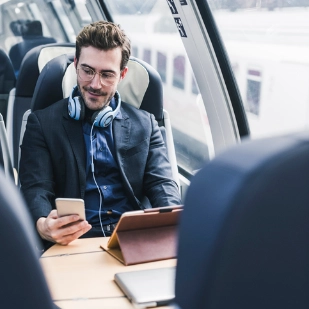 Homme d’affaires assis dans un train qui consulte son téléphone portable et sa tablette.  