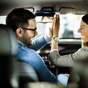 Un couple heureux assis à l’intérieur de leur nouvelle voiture et se donnant un high-five.