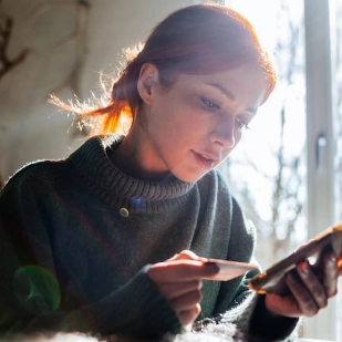 Une femme regarde son smartphone en tenant une carte bancaire
