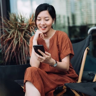 Une femme assise, regarde son smartphone en souriant