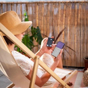 femme assise sur une chaise longue, regarde son smartphone en tenant une carte bancaire