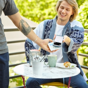 Jeune homme effectuant un paiement sans contact avec un smartphone dans un café.