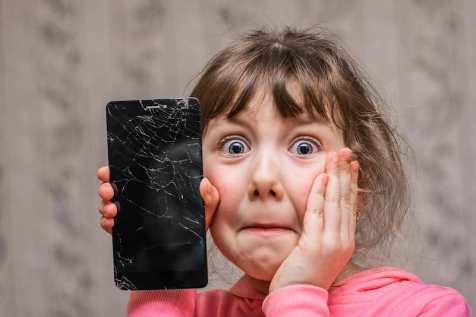 Une petite fille tient un téléphone cassé