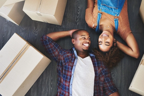 Deux personnes se sourient, allongées sur le sol, au milieu de cartons de déménagement