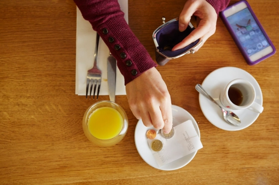Une personne laisse de la monnaie dans une soucoupe, un verre de jus et une tasse de café vide sont visible à côté