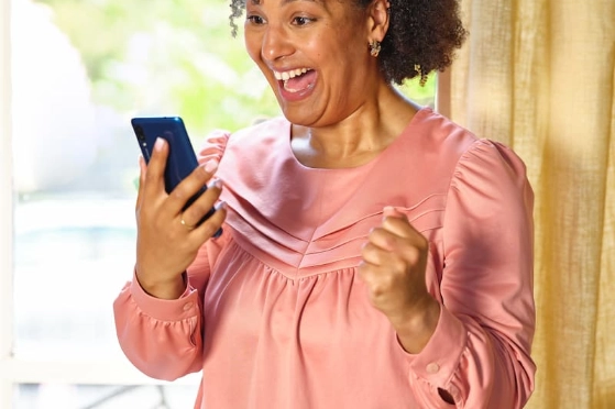 Une femme regarde son smartphone en éclatant de joie