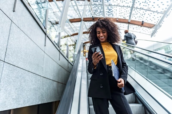 Une femme change de banque en depuis son smartphone en descendant un escalator