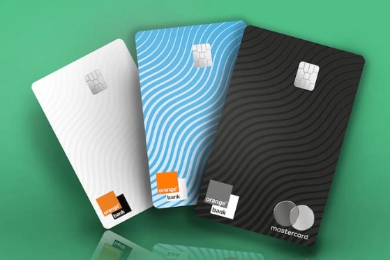 Cartes bancaires Orange Bank posées dans l'herbe : carte premium, standard et carte Plus. 