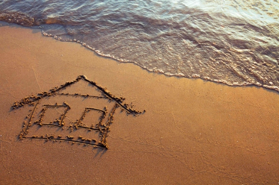 une maison est dessinée dans le sable, au bord de la mer 