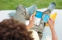 Adolescent allongé sur l'herbe qui consulte son compte bancaire Orange Bank avec une application mobile. 