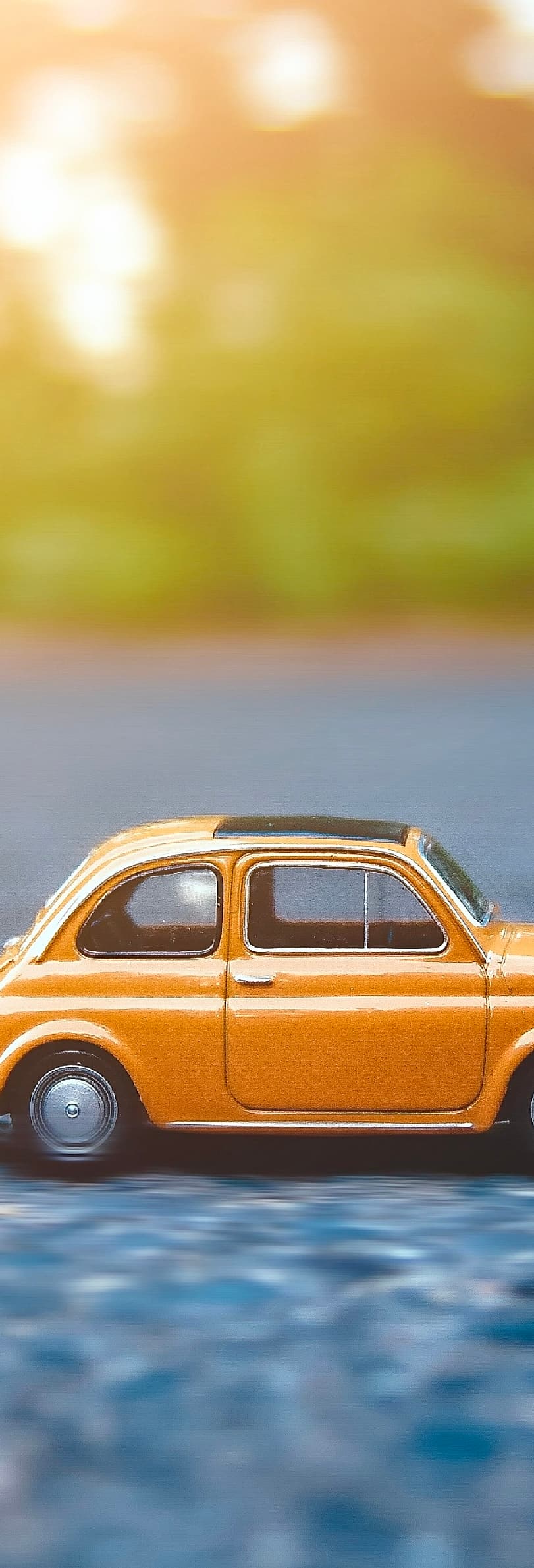 Un vieux modèle jaune de Fiat 500 jouet est posé sur la route