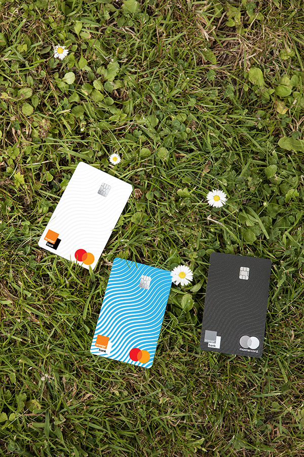 Carte Premium, carte Plus et carte Standard Orange Bank posées dans l'herbe.  