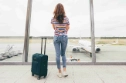 Une femme avec une valise à un aéroport, regarde un avion arrêté sur la piste, elle est de dos