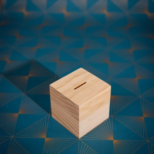 Une tirelire en bois et en forme de cube est posée sur un fond bleu